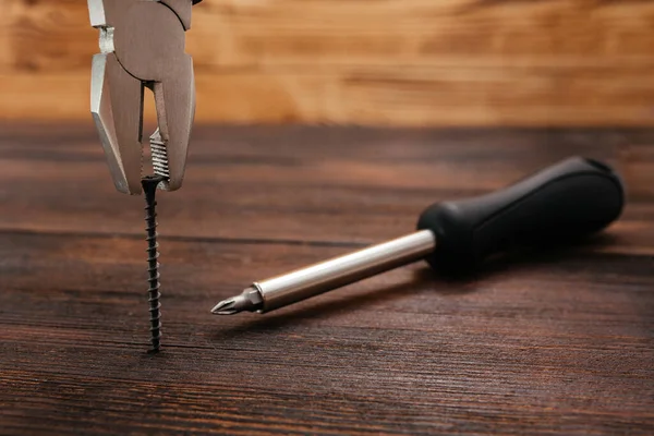 Een man met een tang trekt een zelftappende schroef uit een donker hout. Reparatie van uw eigen huis. — Stockfoto