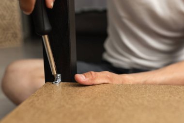 Sıradan kıyafetler giymiş bir adam tornavidayla masaya vida sokuyor. Yakın plan. Aile günlük hayatı.