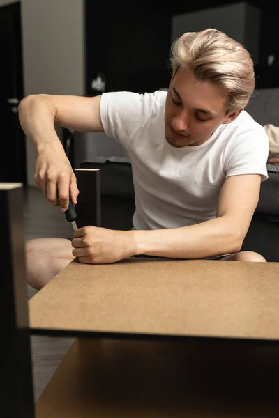 En man reparerar bordsben med en skruvmejsel i vardagsrummet. Familjens vardag. — Stockfoto