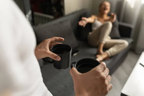 Chlápek přinese dva džbány čaje ženě ležící na gauči. Detailní záběr hrnků s pitím. — Stock fotografie