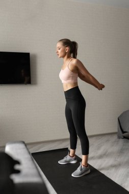 Spor giyimli beyaz kadın antrenmana başlamadan önce evde ısınıyor. Sağlıklı yaşam tarzı ve vücudunu izlemek.
