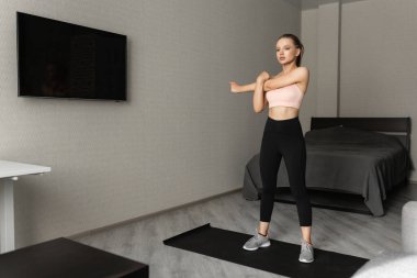 Spor giyimli beyaz kadın antrenmana başlamadan önce evde ısınıyor. Sağlıklı yaşam tarzı ve vücudunu izlemek.