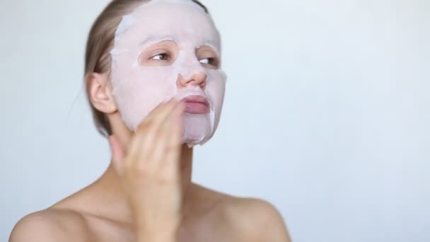 Mooi meisje zet een cosmetisch masker op haar gezicht. Huidverzorging. Maskerblad — Stockvideo