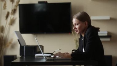 Kız evden uzaktan kumandalı bir bilgisayarla çalışıyor. Elinde not defteriyle.
