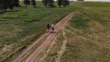 Kır yolunda köpekle koşan bir çift. İnsansız hava aracının üst görünümü.