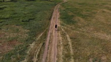 Kadınlar bir kır yolunda köpekle doğada koşuyorlar. İnsansız hava aracının üst görünümü.