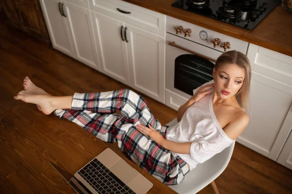 Kaukasische vrouw zit in de keuken aan tafel naast een laptop. — Stockfoto