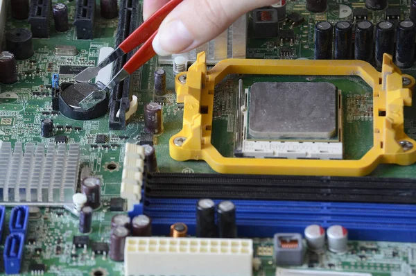 The process of fixing the green motherboard. Repairing an old chip on a computer against a dusty background.