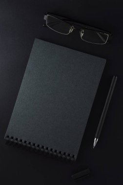 Çalışma alanı - yazmak için bir not defteri, siyah bir arka plan üzerinde bir kalem ve gözlük. Çalışma alanı kavramı