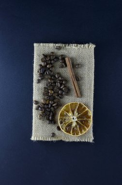 Burlap taze doğal kahve çekirdekleri tarçın çubukları, dilimlenmiş portakal dilimleri ile koyu mavi bir arka plan üzerinde yalan