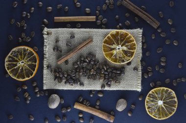 Taze doğal kahve çekirdekleri tarçın çubukları, dilimlenmiş portakal dilimleri ile koyu mavi bir arka plan üzerinde dağınık