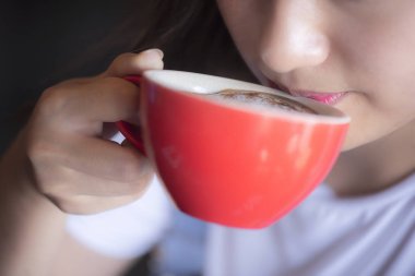 Kırmızı fincanla kahve içen genç bir kadın.