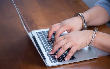 Bilgisayarın klavyesinde elleri kelepçeli, elektronik suç konsepti.