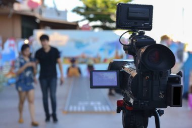 Önünde aktörlerin yürüdüğü canlı video yayını kullanan bir kamera.