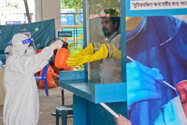 Sağlık çalışanı, 23 Haziran 2020 'de Bangladeş, Dhaka' da Coronavirus salgını devam ederken, Mugda Tıp Fakültesi ve Hastanesi 'nde yaşayan bir hastadan burun çubuğu örneği aldıktan sonra dezenfektan püskürtüyor.
