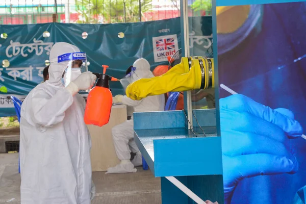 Sağlık çalışanı, 23 Haziran 2020 'de Bangladeş, Dhaka' da Coronavirus salgını devam ederken, Mugda Tıp Fakültesi ve Hastanesi 'nde yaşayan bir hastadan burun çubuğu örneği aldıktan sonra dezenfektan püskürtüyor.