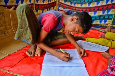 Rohingya mülteci çocukları yazarken ve diğer çocuklar, 06 Eylül 2017 'de Bangladeş, Cox' s Bazar 'daki Thengkhali derme çatma kamplarında uyuyorlar. 600.000 'den fazla Rohingya askeri baskından bu yana Bangladeş' e geldi.
