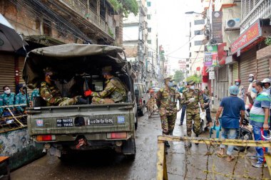 Bangladeş Ordusu askerleri ve polisi, Bangladeş 'in başkenti Dhaka' da bulunan Wari 'de, 4 Temmuz 2020' de hükümet tarafından azami enfeksiyon riski bulunan koronavirüs kırmızı bölgesinde devriye gezerken evlerinde kalacaklarının farkında.