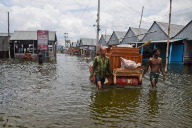 7 Ağustos 2020 'de Dhaka, Bangladeş yakınlarındaki sel basmış caddelerden mobilyalarıyla geçen köylüler,