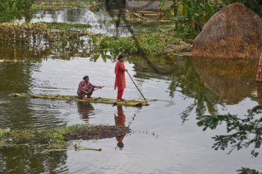 7 Ağustos 2020 'de Bangladeş, Dhaka yakınlarındaki Savar' daki sel sularında muz ağaçlarından yapılmış derme çatma bir sala binen köylü kadın görülüyor.