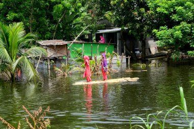 10 Ağustos 2020 'de Bangladeş, Dhaka yakınlarında Savar' daki sel sularında muz ağaçlarından yapılmış derme çatma bir sala binen köylü kızlar görülüyor.
