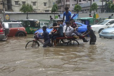 26 Temmuz 2017 'de sağanak yağış neredeyse durgunluğa yol açtıktan sonra, vatandaşlar Dhaka' nın sel basmış sokaklarında yürüyor. Şiddetli muson yağmurlarının ardından Bangladeş 'in başkenti Dhaka' nın büyük bölümü sular altında kaldı.. 