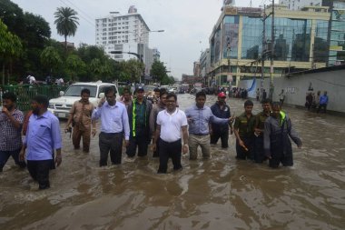 26 Temmuz 2017 'de sağanak yağış neredeyse durgunluğa yol açtıktan sonra, vatandaşlar Dhaka' nın sel basmış sokaklarında yürüyor. Şiddetli muson yağmurlarının ardından Bangladeş 'in başkenti Dhaka' nın büyük bölümü sular altında kaldı.. 
