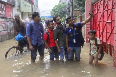 26 Temmuz 2017 'de sağanak yağış neredeyse durgunluğa yol açtıktan sonra, vatandaşlar Dhaka' nın sel basmış sokaklarında yürüyor. Şiddetli muson yağmurlarının ardından Bangladeş 'in başkenti Dhaka' nın büyük bölümü sular altında kaldı.. 