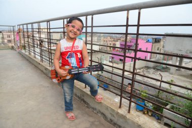 11 Nisan 2020 'de Bangladeş' in Dhaka kentindeki COVID-19 Coronavirus 'a karşı tedbir olarak hükümet tarafından uygulanan tecrit sırasında bir binanın çatısında oyuncak gitar çalan bir çocuk.