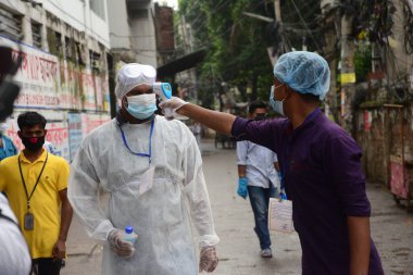 Gönüllü, 13 Haziran 2020 'de Bangladeş' in Dhaka kentindeki Doğu Rajabazar kentindeki azami enfeksiyon riski bulunan hükümete girerken bir asistanın sıcaklığını kontrol ediyor. Yetkililer Doğu Rajabazar 'ı Dhaka' da tamamen tecrit altına aldı. 