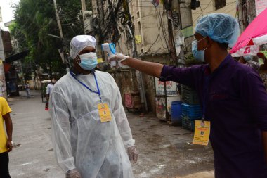 Gönüllü, 13 Haziran 2020 'de Bangladeş' in Dhaka kentindeki Doğu Rajabazar kentindeki azami enfeksiyon riski bulunan hükümete girerken bir asistanın sıcaklığını kontrol ediyor. Yetkililer Doğu Rajabazar 'ı Dhaka' da tamamen tecrit altına aldı. 