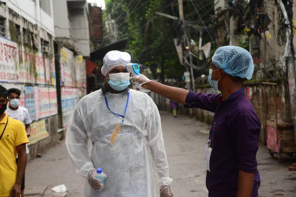 Gönüllü, 13 Haziran 2020 'de Bangladeş' in Dhaka kentindeki Doğu Rajabazar kentindeki azami enfeksiyon riski bulunan hükümete girerken bir asistanın sıcaklığını kontrol ediyor. Yetkililer Doğu Rajabazar 'ı Dhaka' da tamamen tecrit altına aldı. 