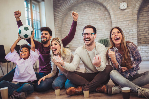 Young friends watching soccer on tv and celebrating victory at home