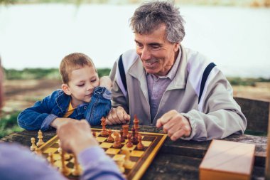 Aktif emekli insanlar, eski arkadaşları ve serbest zaman, eğleniyor ve satranç oynarken parkta, iki üst düzey erkek torunu ile vakit geçirmek