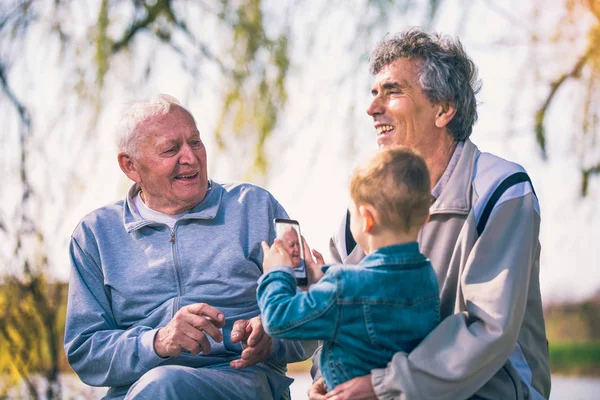 Dwóch Starszych Mężczyzn Wnuka Pomocą Smart Telefonu Parku — Zdjęcie stockowe