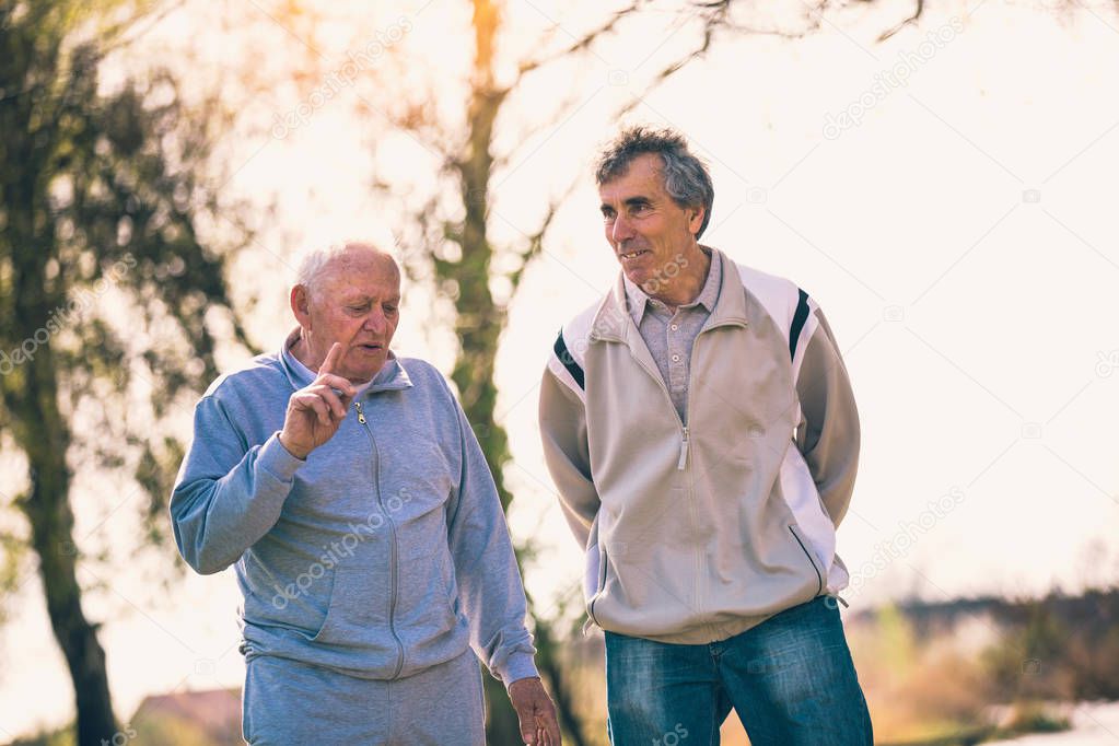 Adult son walking with his senior father in the park.