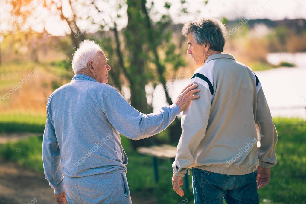 Adult son walking with his senior father in the park.