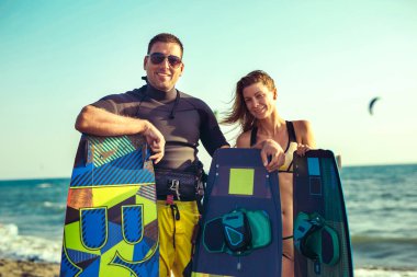 Pretty smiling caucasian woman kitesurfer enjoying summertime on sandy beach with boyfriend. clipart