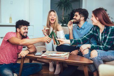 Pizza yemek, bira içme ve evde tv izlerken genç arkadaş grubu.