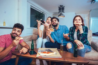 Pizza yemek, bira içme ve evde tv izlerken genç arkadaş grubu.
