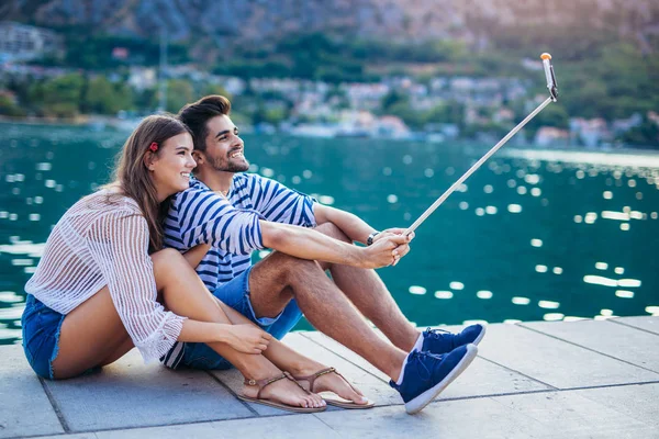 浪漫情侣坐在海上码头 使自拍智能手机和自拍棒 — 图库照片