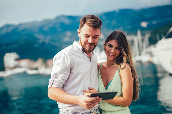 Young couple using digital tablet outdoor against sea boats enjoying summer holidays