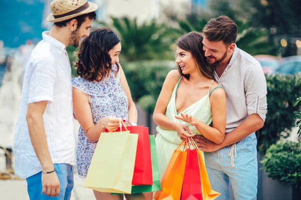 Group of friends with shopping bags walking at harbor of touristic sea resort with boats on background