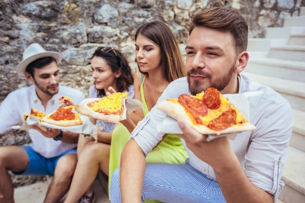Young friends eating pizza in city while travelling