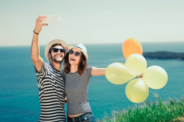 Gülümseyen çift balonlu güneş gözlüğü takmış selfie fotoğraf deniz arka plan üzerinde olun.