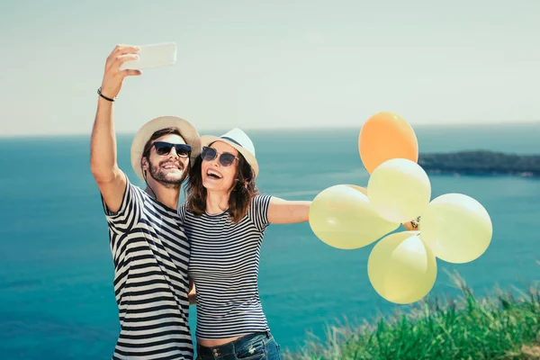 Smilende Par Med Solbriller Med Ballonger Gjør Selfiebildet Havbakgrunn – stockfoto