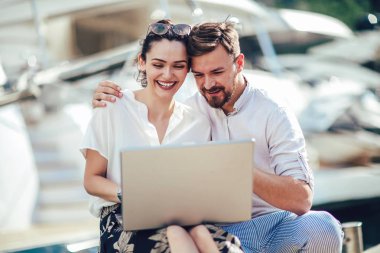 Güzel romantik çift dizüstü bilgisayar kullanarak. Belgili tanımlık laptop resimleri, arka plan üzerinde tekne ile turistik deniz tatil liman tarafından seyahat ederken izlerken.