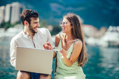 Güzel romantik çift dizüstü bilgisayar kullanarak. Belgili tanımlık laptop resimleri, arka plan üzerinde tekne ile turistik deniz tatil liman tarafından seyahat ederken izlerken.