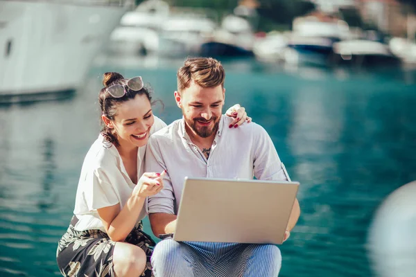 Güzel romantik çift dizüstü bilgisayar kullanarak. Belgili tanımlık laptop resimleri, arka plan üzerinde tekne ile turistik deniz tatil liman tarafından seyahat ederken izlerken.