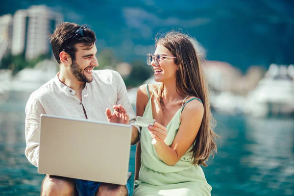 Güzel romantik çift dizüstü bilgisayar kullanarak. Belgili tanımlık laptop resimleri, arka plan üzerinde tekne ile turistik deniz tatil liman tarafından seyahat ederken izlerken.